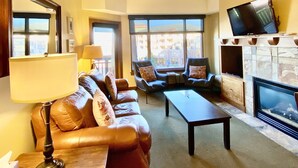 Ein Wohnzimmer mit einer Sofagarnitur, einem Couchtisch, einem Kamin und einem an der Wand befestigten Fernseher.
