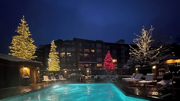 Ein Schwimmbecken mit drei beleuchteten Weihnachtsbäumen und Liegestühlen darum herum.