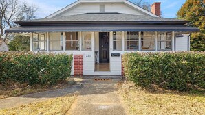 A single-story house with a gabled roof, a front porch with a bench, and a number '2211' on the door. - Bohemian Styled Home with Bonus Game Room (Kannapolis)