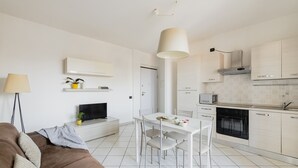 A modern kitchen with white cabinetry, a dining area with a white table and chairs, a flat-screen TV, and a pendant light. - HQ Aparthotel Milano Inn - Smart Suites -  Standard one bedroom Apartment (Cinisello Balsamo)