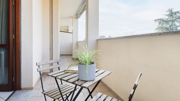 A balcony with a wooden table and chairs, a potted plant, and a view of the sky and trees. - HQ Aparthotel Milano Inn - Smart Suites -  Standard one bedroom Apartment (Cinisello Balsamo)