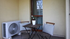Ein kleiner Sitzbereich im Freien mit Tisch und zwei Stühlen, einem Blumentopf und einer Klimaanlage.