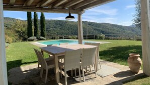 Une terrasse couverte avec une piscine, des meubles en osier et une vue sur un paysage montagneux.