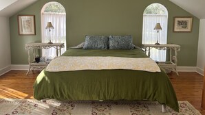 Une chambre avec un mur vert, un lit recouvert d’une literie à motifs, deux tables de chevet avec des lampes et une fenêtre donnant sur un paysage agréable.
