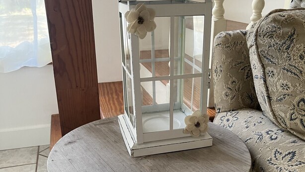 Une lanterne blanche, ornée de motifs floraux, posée sur une table ronde en bois.