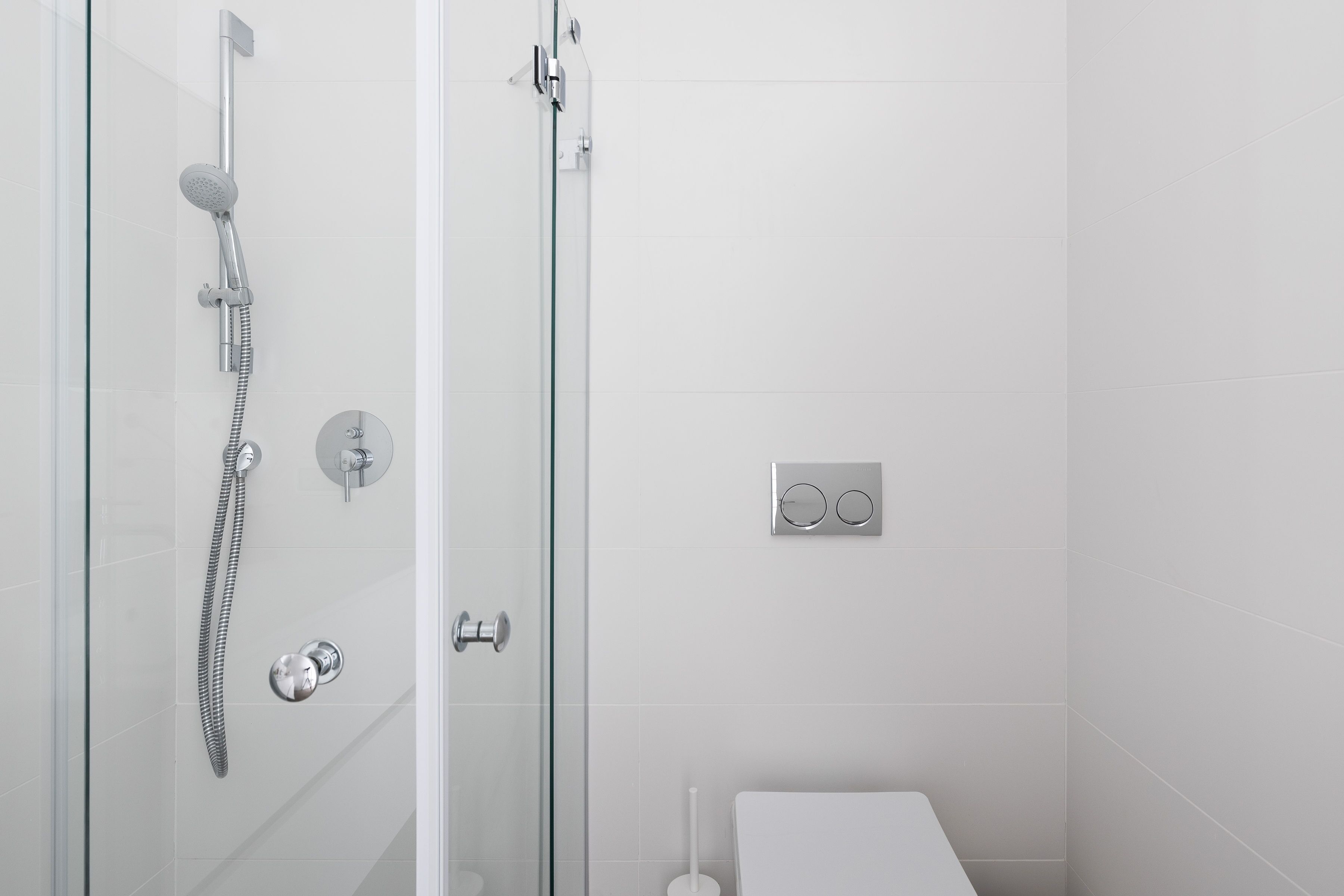 A modern bathroom with a glass shower enclosure, a toilet, and a wall-mounted flush handle.