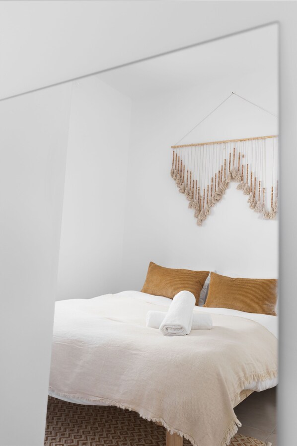 A minimalist bedroom with a bed, a macrame wall hanging, and patterned floor tiles. - Elegant 2BD Apartment in Jaffa Area (Tel Aviv)