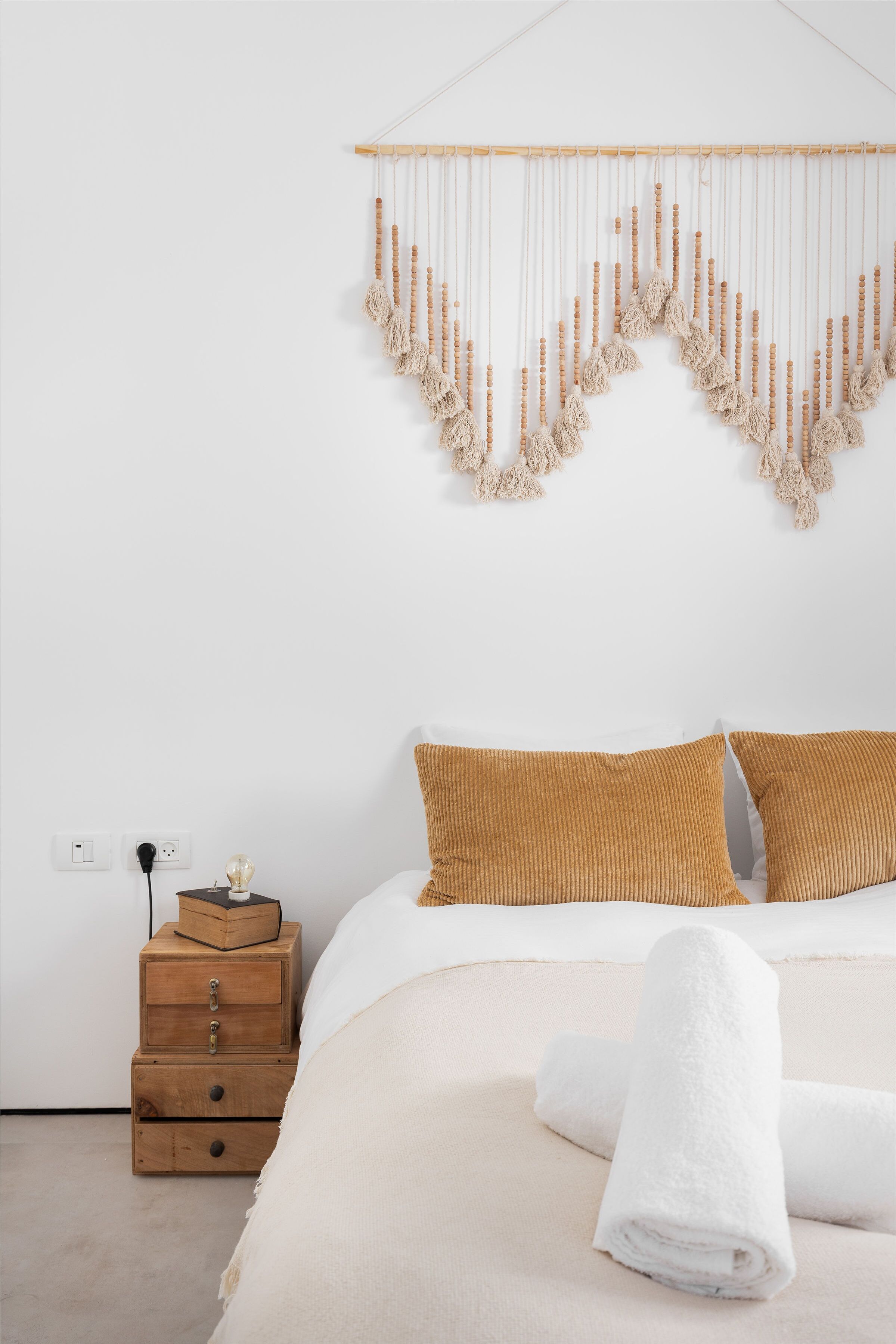 Un dormitorio ordenado con una cama, dos mesitas de noche de madera, un adorno en la pared y una toalla blanca sobre la cama.