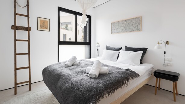 A minimalist bedroom with a bed, a ladder, a window, and a bedside table. - Elegant 2BD Apartment in Jaffa Area (Tel Aviv)