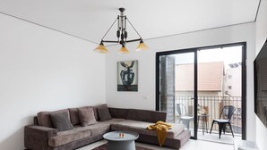 A modern living room with a grey sectional sofa, a round coffee table, and a large window with a balcony. - Elegant 2BD Apartment in Jaffa Area (Tel Aviv)