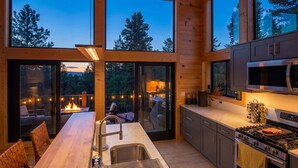 A modern kitchen with large windows, a dining area, and a view of a fire pit outside. - Lakefront - Alpine Views - Daily Moose (Black Hawk)
