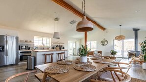 A spacious kitchen with modern appliances, a wooden dining table with woven placemats, and a large window providing natural light. - The Blue Cactus Ranch - Pool and Spa (Joshua Tree)