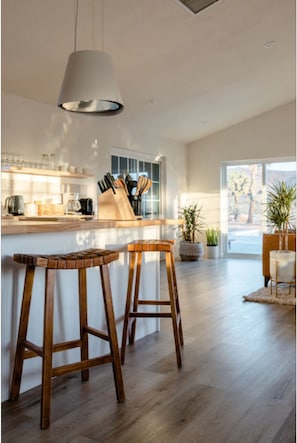 Uma cozinha moderna com banquetas de madeira, luminária pendente e vista para o exterior.