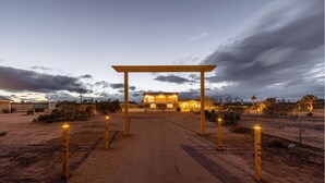 A desert landscape with a paved pathway leading to a building with a wooden pergola entrance. - The Blue Cactus Ranch - Pool and Spa (Joshua Tree)