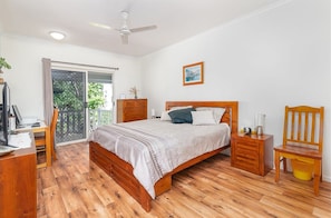 Un dormitorio con una cama de madera, un escritorio, una silla, una mesita de noche y una ventana con cortinas.