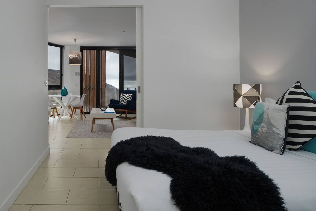 Moderni hotellihuone, jossa on suuri sänky, työpöytä ja tuoli. Ikkunoista on näkymä ulos.