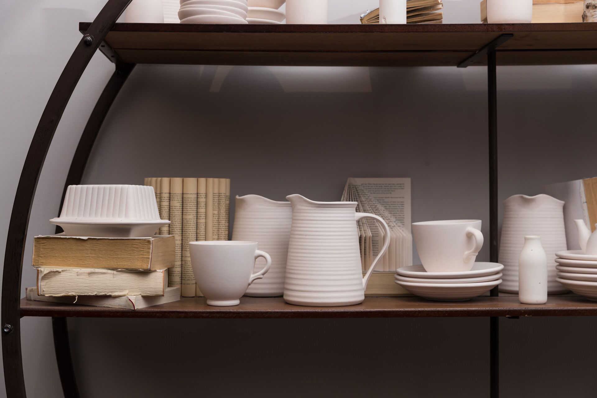 Une étagère sur laquelle sont disposés divers objets en céramique blanche, notamment un pichet, des tasses et des assiettes.