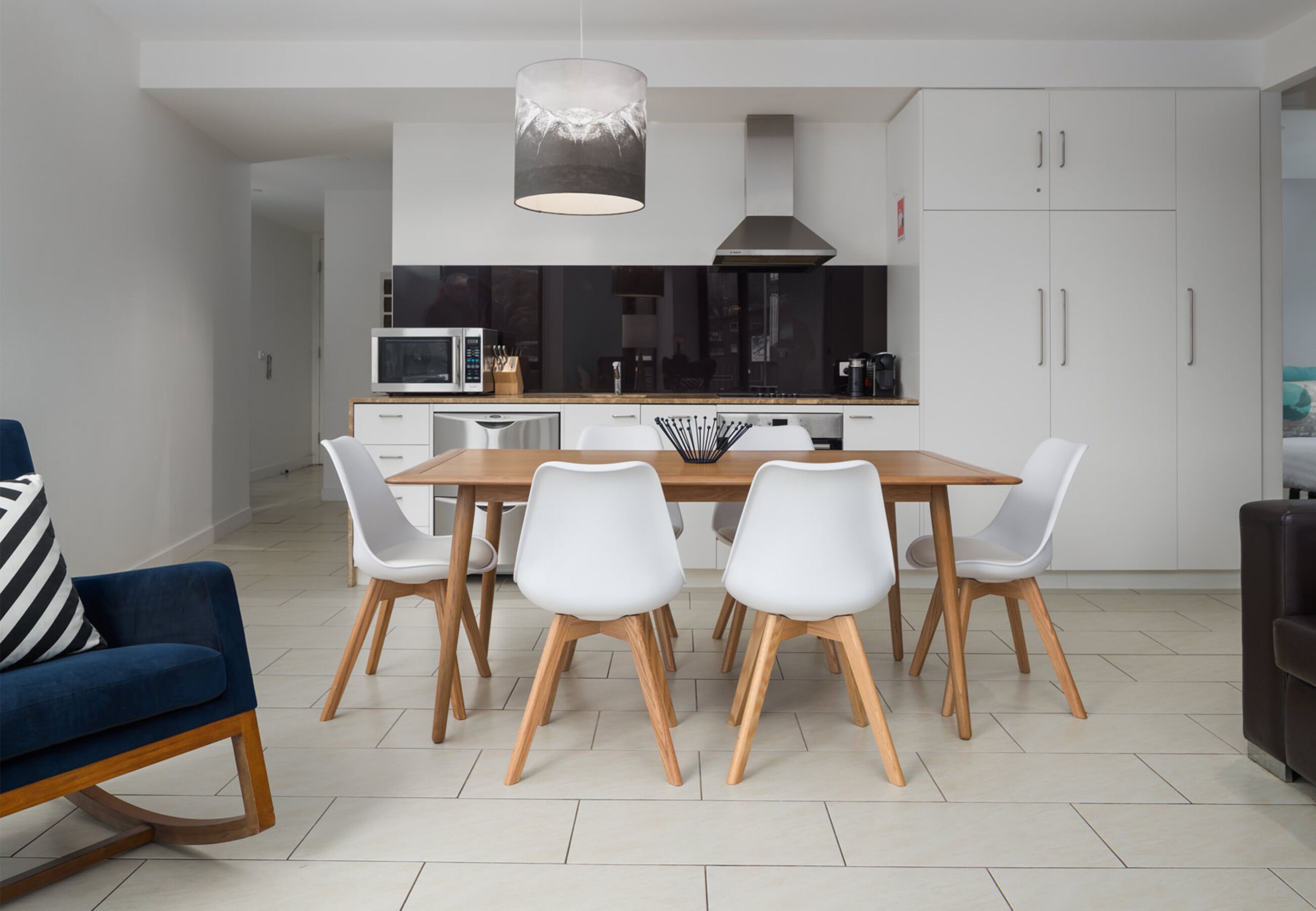 Una cocina moderna con armarios blancos, una mesa de comedor de madera y sillas blancas.