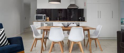 Una cocina moderna con armarios blancos, una mesa de comedor de madera y sillas blancas.