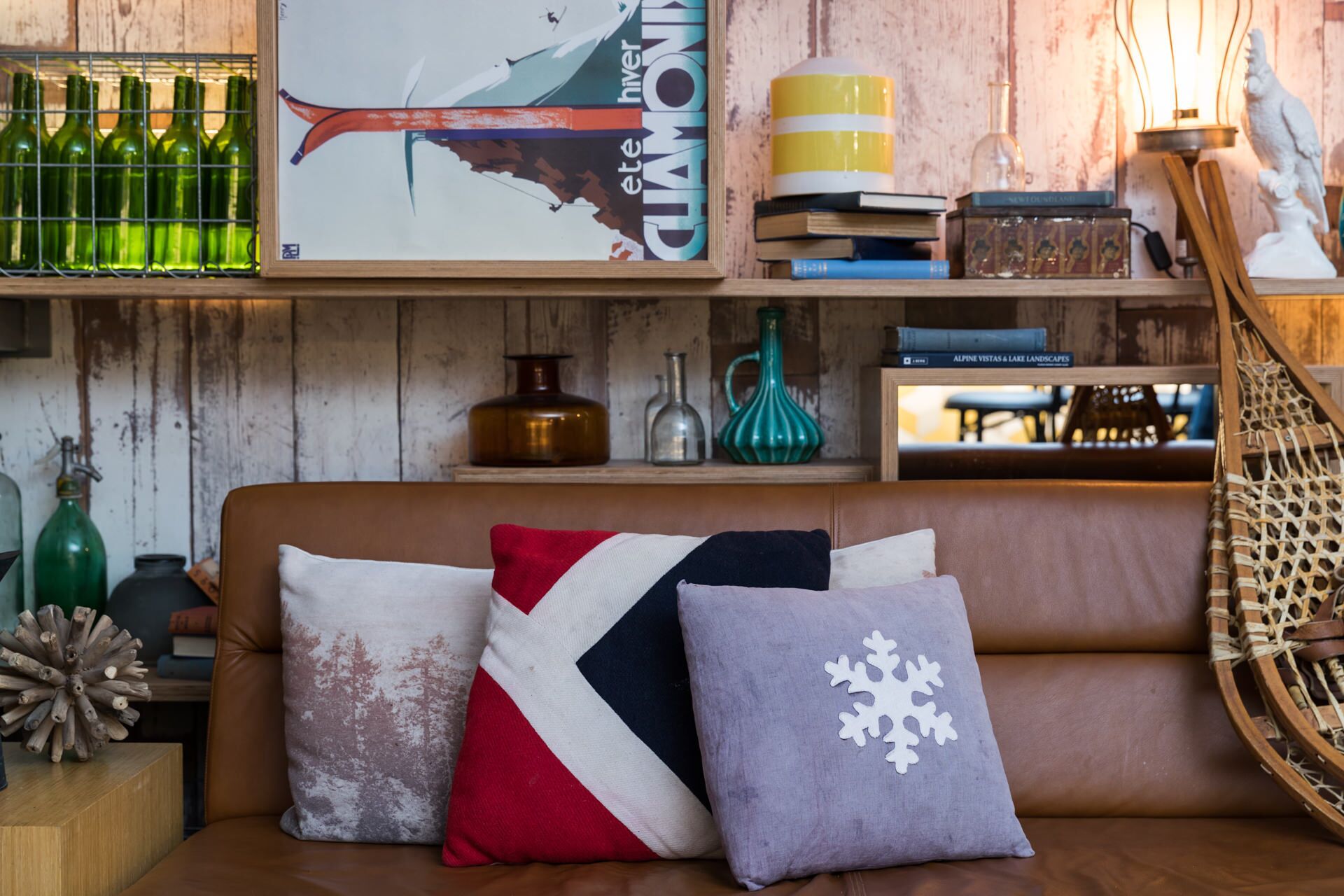 A cozy room with a wooden wall, a brown leather sofa, and decorative pillows.