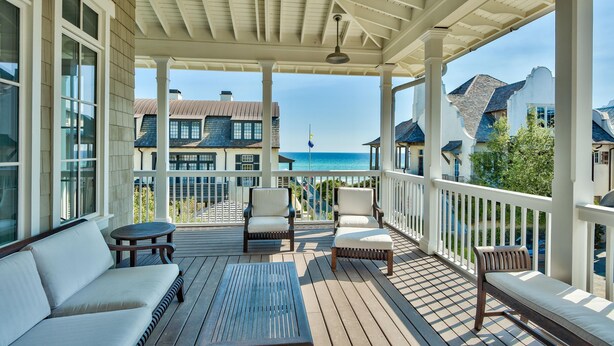 A covered outdoor deck with seating, a view of the ocean, and a building in the background.