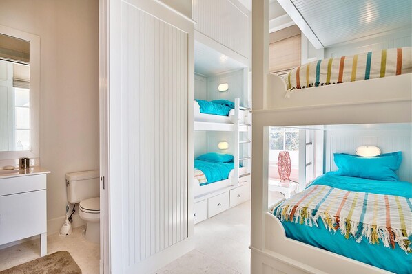 A bedroom with bunk beds, a white wardrobe, a bathroom with a toilet, and a window with a view. - Looking Glass Cottage & Carriage House (Rosemary Beach)