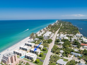 An aerial view of a coastal residential area with beachfront properties, a road, and a boat on the water.