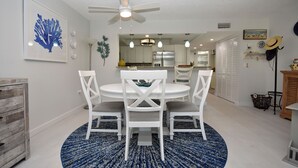 Un coin repas avec une table et des chaises blanches, un ventilateur de plafond et un tapis à motifs bleus.