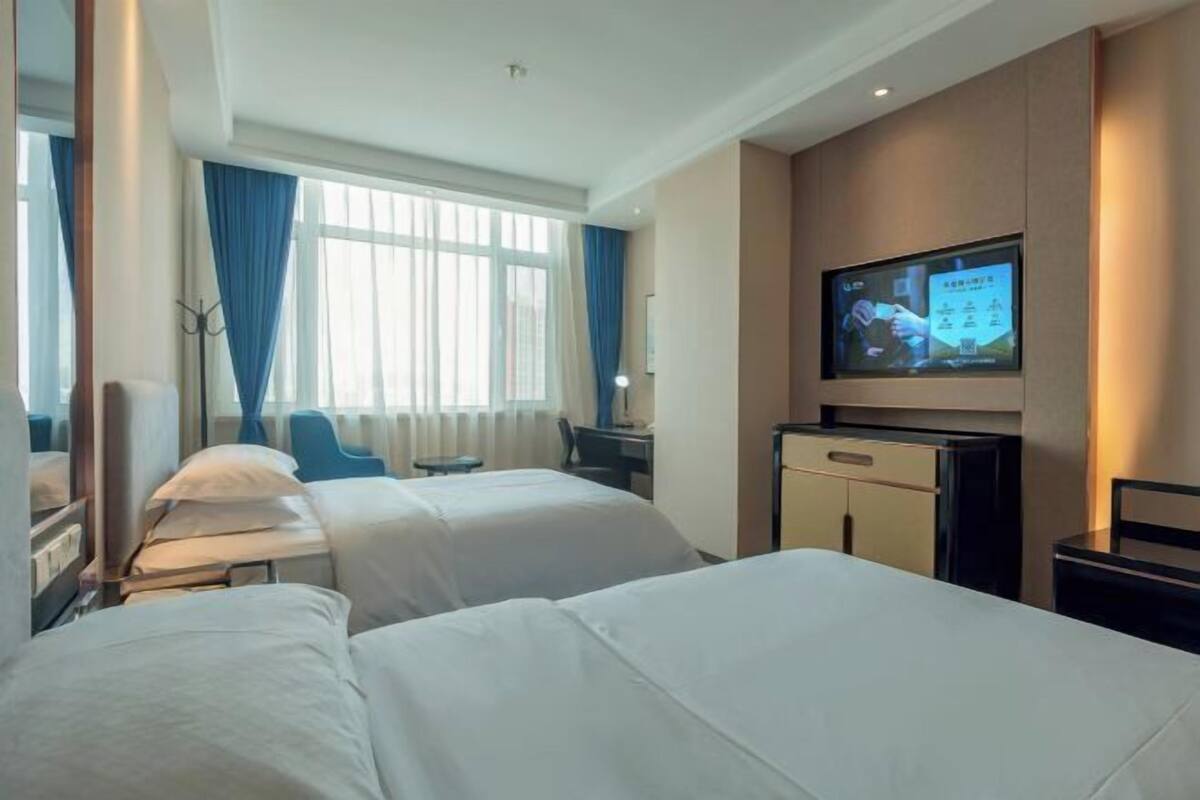 A hotel room with two beds, a television, a desk, and a chair.