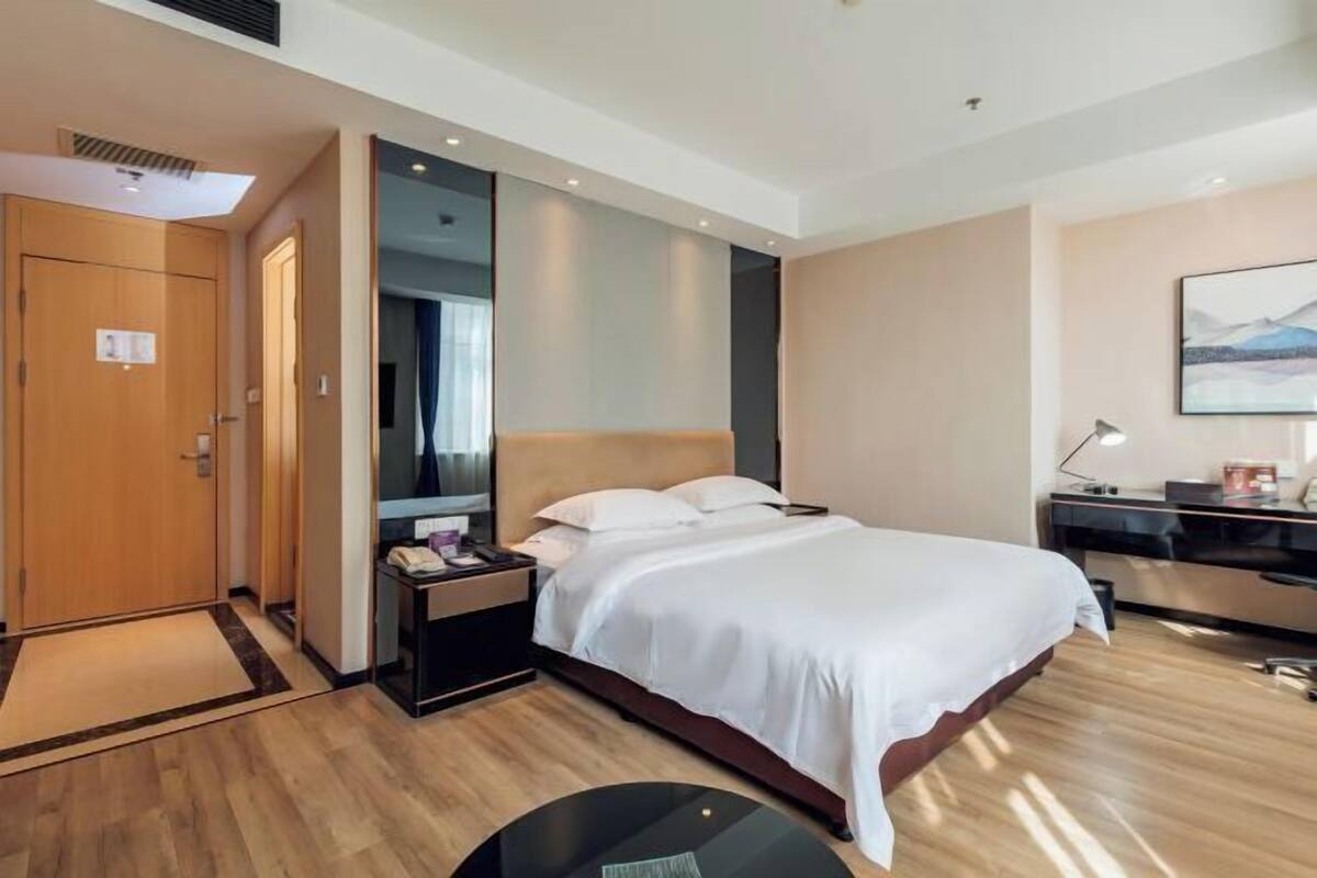 A hotel room with a bed, a desk, a chair, a nightstand, and a mirror.