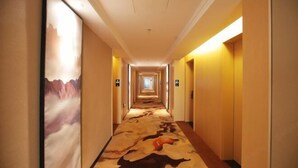 Un pasillo de hotel con alfombra que presenta un diseño de paisaje montañoso, un techo de color claro y una serie de puertas a ambos lados.