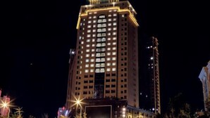 Un edificio de hotel alto e iluminado, con varios pisos y ventanas, rodeado de árboles y farolas.