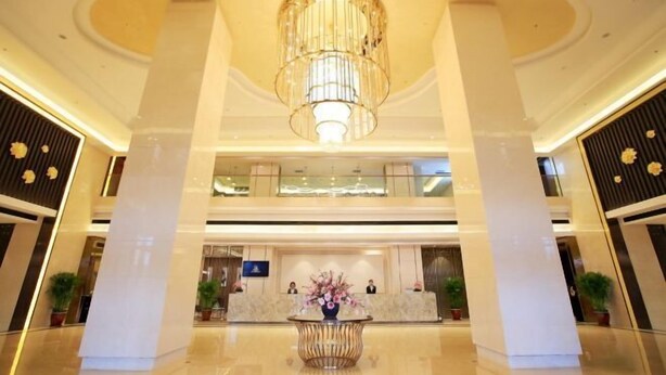 Un hall de hotel con una recepción central, una araña y un suelo pulido.