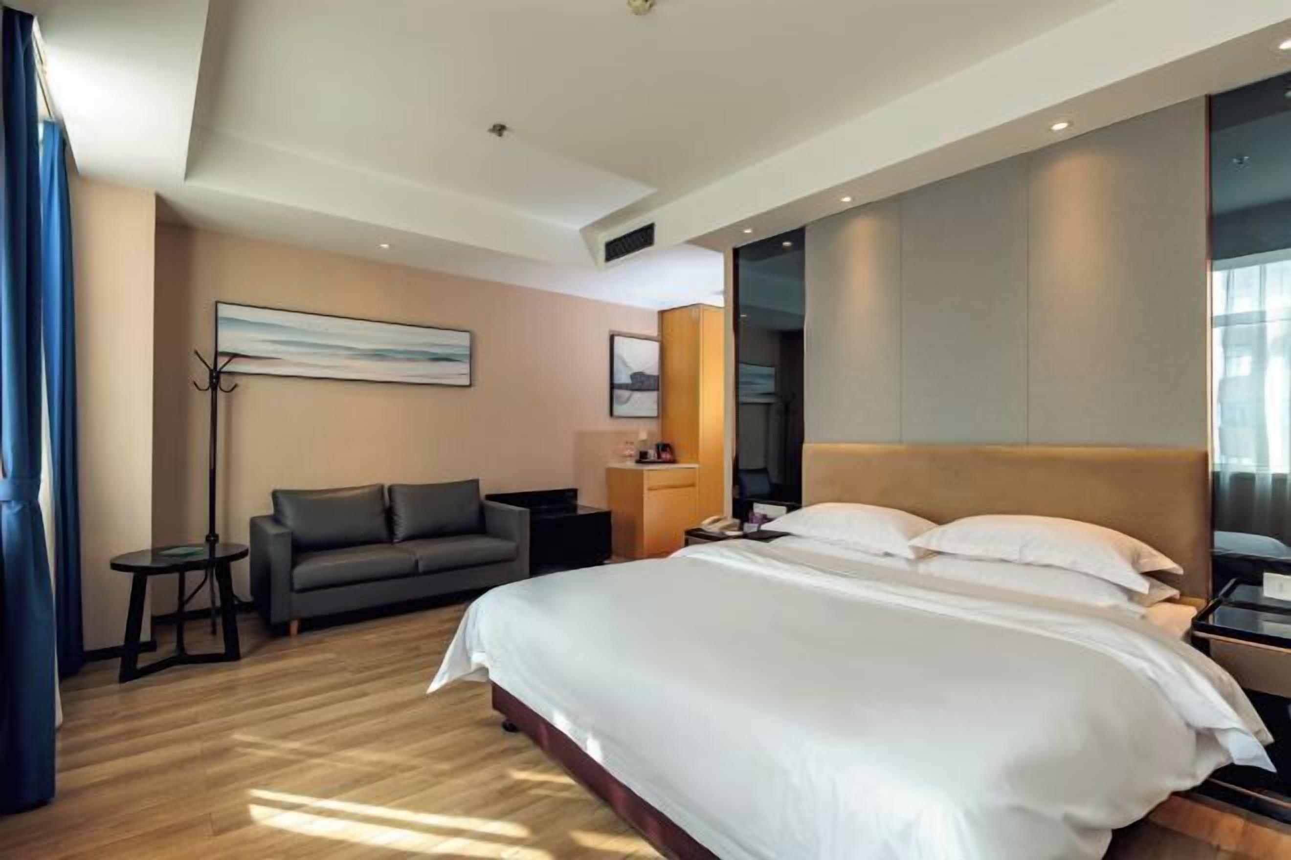 Una camera d'albergo moderna con un letto grande, un divano, una scrivania e una lampada da terra.