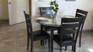 Et spiseområde med et rundt bord, fire stole, en vase med blomster og et fastgjort elektrisk dåre.