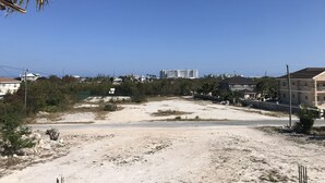 Et sandet område med sparsom vegetation, en vej og boliger i baggrunden.
