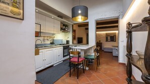 A kitchen with white cabinets, a dining area with chairs, a hanging light fixture, and a tiled floor.