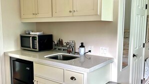 A compact kitchen with white cabinetry, a built-in microwave, a sink, and a dishwasher.
