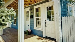 A house with a covered porch, a front door, and a small garden area with a tree and a flower basket.