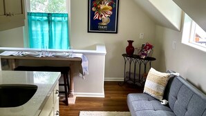 A kitchen with a dining area, a gray sofa, and a framed artwork on the wall.