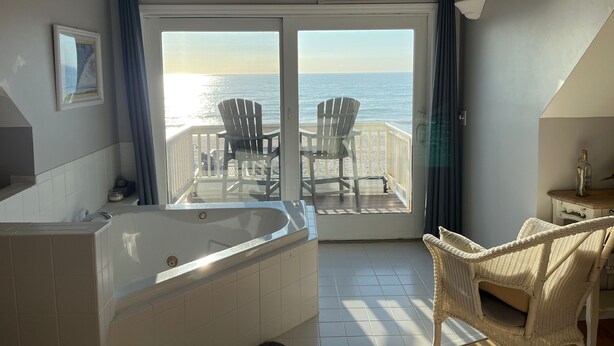 A room with a large bathtub, a television, and a view of the ocean through a sliding door. - Beach Front with Charm and Luxury. 2 person Hot Tub on Deck. Beautiful Loft! (North Topsail Beach)