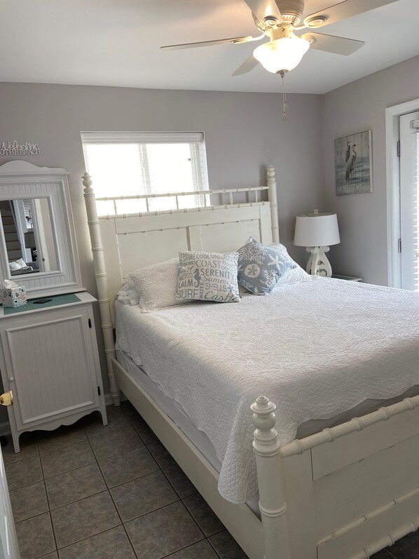 A neatly arranged bedroom with a white bed, a nightstand, a dresser, and a ceiling fan. - Beach Front with Charm and Luxury. 2 person Hot Tub on Deck. Beautiful Loft! (North Topsail Beach)