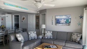 A living room with a grey sectional sofa, a wooden coffee table, and a ceiling fan. - Beach Front with Charm and Luxury. 2 person Hot Tub on Deck. Beautiful Loft! (North Topsail Beach)