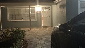 En uppfart som leder till ett hus med en garageport, en krukväxt och en bil parkerad på höger sida.