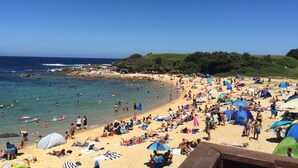 Une plage bondée, où l’on voit des gens bronzer et se baigner, ainsi que des tentes et des parasols.