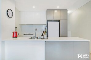 Une cuisine moderne avec des meubles blancs, un réfrigérateur en acier inoxydable, un évier et une horloge au mur.