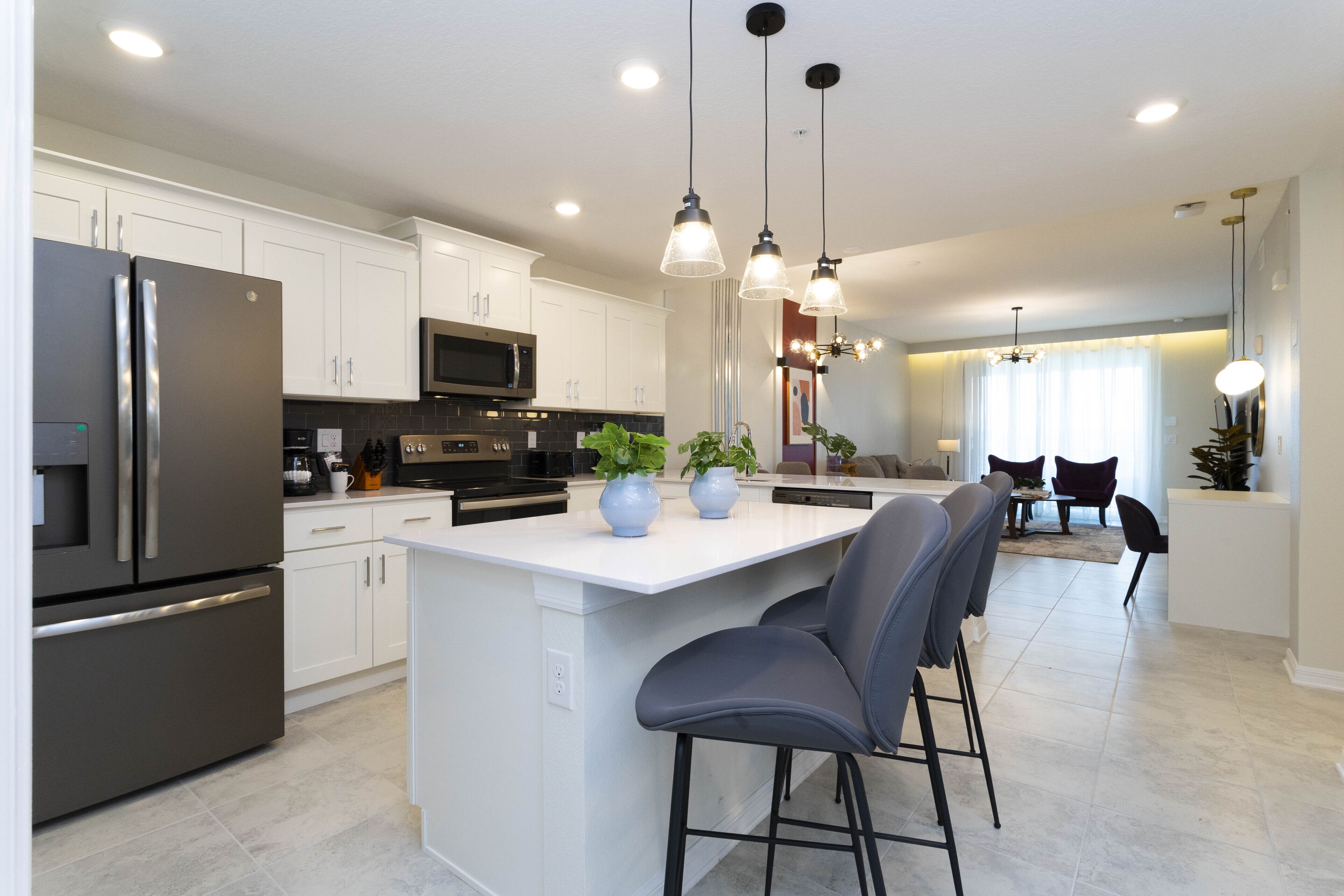 Una cocina moderna con armarios blancos, electrodomésticos de acero inoxidable y una isla central con taburetes de bar.