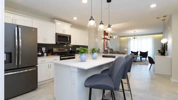 Una cocina moderna con armarios blancos, electrodomésticos de acero inoxidable y una isla central con taburetes de bar.