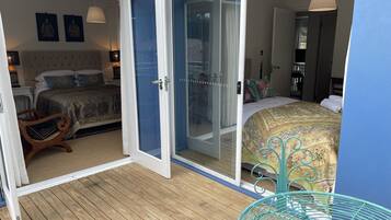 A bedroom with a large bed, a wooden floor, and a sliding glass door leading to a balcony.