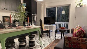 A modern living room with a green dining table, black stools, a patterned rug, a black sofa, and a TV in the background. - TREETOPS PENTHOUSE ROSE BAY, SYDNEY 3 BEDROOMS LOUNGE KITCHEN/GARAGE PARKING (Rose Bay North)